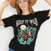 Women in a keep it wild graphic tee holding a hat she wearing