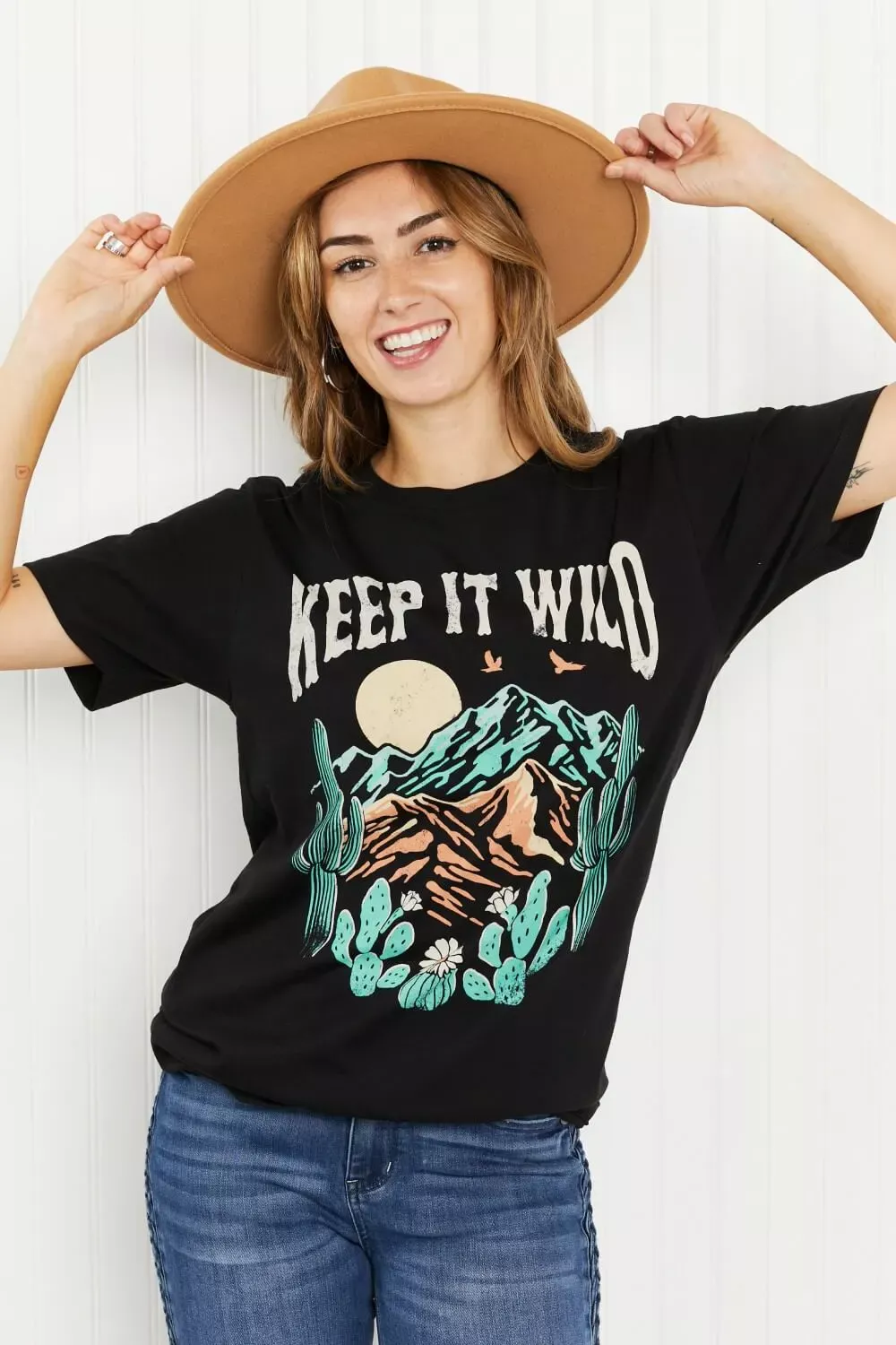 Women in a keep it wild graphic tee holding a hat she wearing